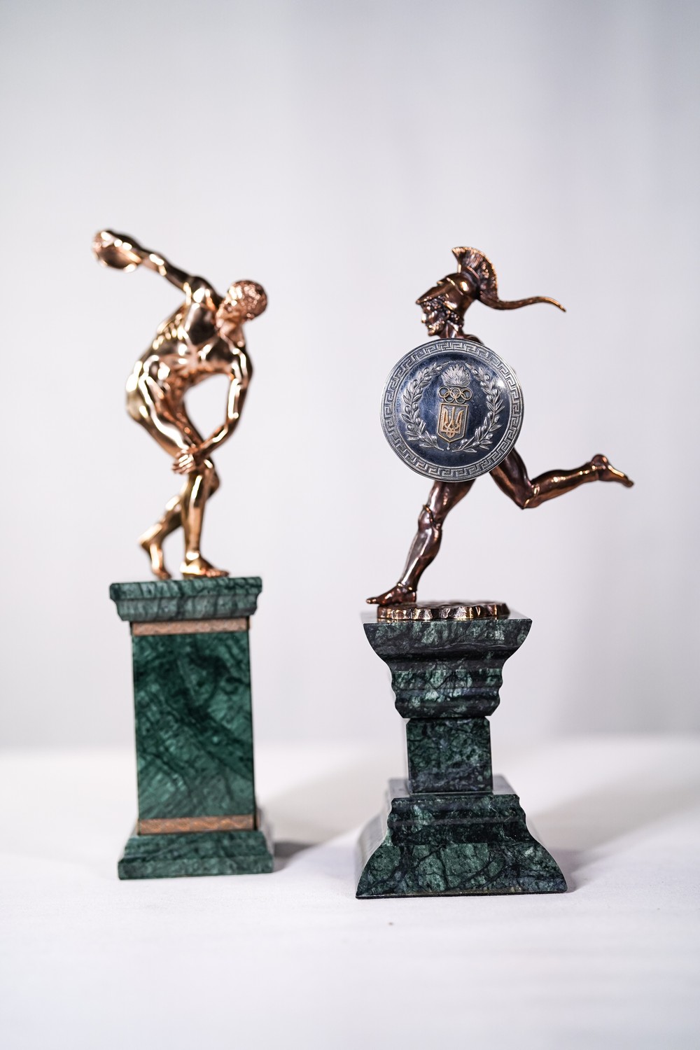 Скульптурні фігури «Дискоболу» (метальника диску) та «Факелоносця олімпійського вогню» з щитом НОК України в давньогрецькій стилістиці. 2000 – ті роки. Малахіт бронза